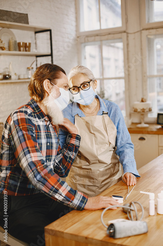 Old couple in a kitchen. Woman in a blue shirt and aprone. People in a medical masks. photo