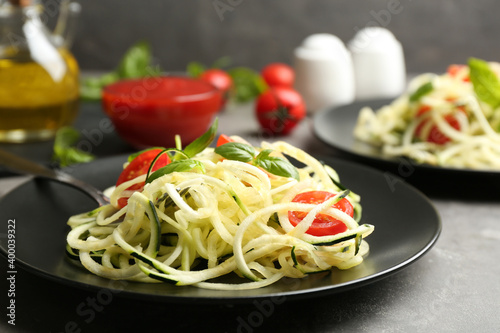 Delicious zucchini pasta with cherry tomatoes and basil on light grey table, closeup