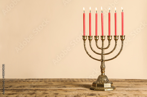 Golden menorah with burning candles on wooden table against beige background, space for text