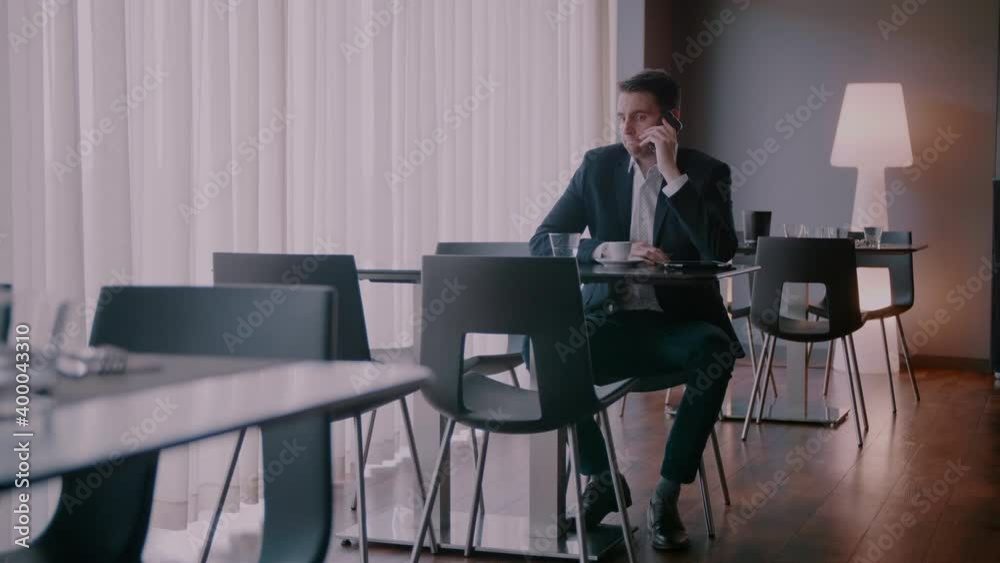 Businessman sitting at a table and being in doubt while talking on the phone Businessman sitting at a table and being in doubt while talking on the phone