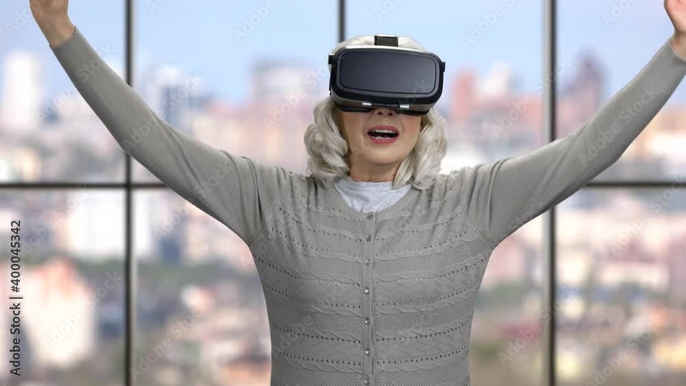 Mature woman wearing virtual reality headset. Senior woman using vr glasses on windows background. Modern technology concept.