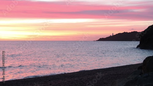 Waves lapping on beach looking at Start Point Lighthouse, Devon. photo