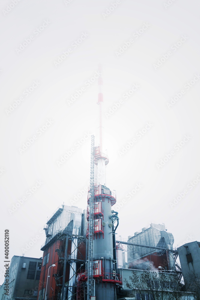 Chimney at heating plant covered in fog, cloudy winter day, low angle view, energy production, air pollution, climate change and global warming concept Chimney at heating plant covered in fog, cloudy winter day, low angle view, energy production, air pollution, climate change and global warming concept