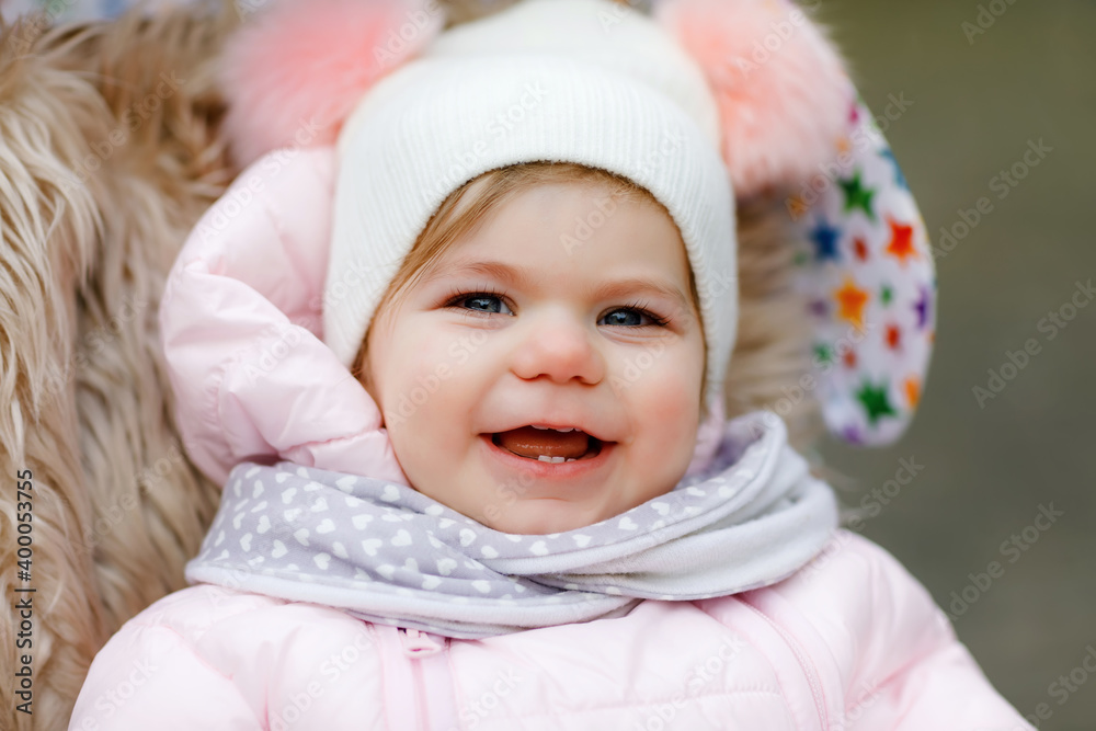 Cute little beautiful baby girl sitting in the pram or stroller on cold autumn, winter or spring day. Happy smiling child in warm clothes, fashion stylish baby coat and hat. Snow falling down Cute little beautiful baby girl sitting in the pram or stroller on cold autumn, winter or spring day. Happy smiling child in warm clothes, fashion stylish baby coat and hat. Snow falling down