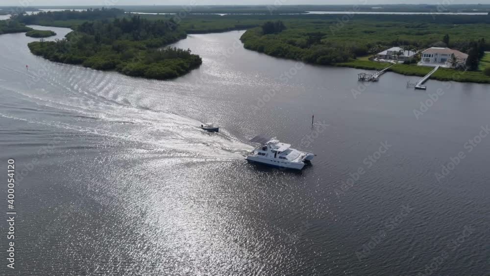 Luxury catamaran and small motorboat cruising out of harbor of Vero Beach. Sun reflection in the water. Aerial circling view. Luxury catamaran and small motorboat cruising out of harbor of Vero Beach. Sun reflection in the water. Aerial circling view.
