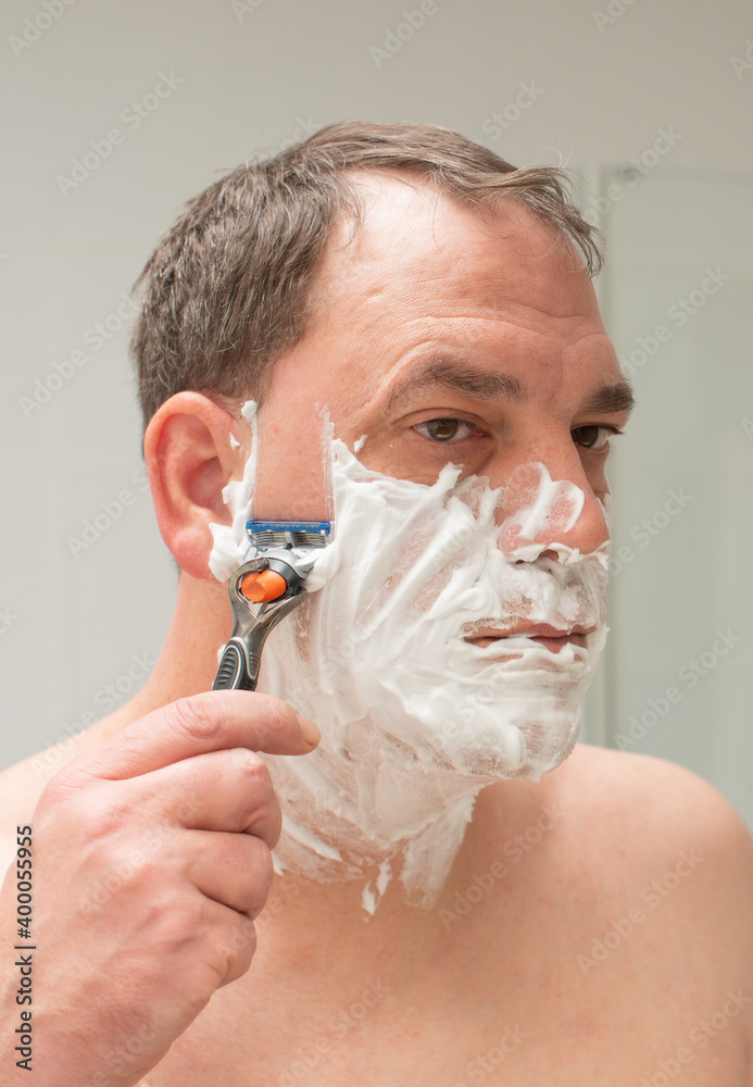 Mann vor einem Spiegel beim Bart rasieren und Gesichtspflege