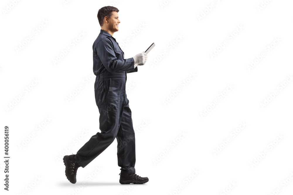 Young male worker in an overall uniform holding a clipboard and walking isolated on white background