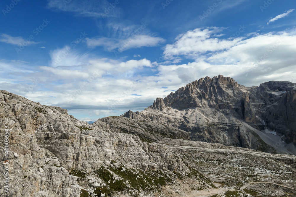 A panoramic view on a high and desolated mountain peaks in Italian Dolomites. The lower parts of the mountains are overgrown with moss and grass. Raw and unspoiled landscape. A bit of overcast.
