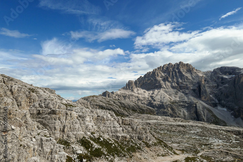 A panoramic view on a high and desolated mountain peaks in Italian Dolomites. The lower parts of the mountains are overgrown with moss and grass. Raw and unspoiled landscape. A bit of overcast.