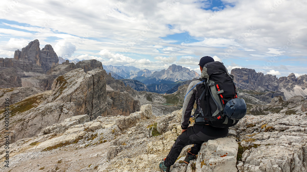 A man hiking in high and desolated mountains in Italian Dolomites. He sits on a big boulder and enjoys the idyllic landscape. Raw and unspoiled landscape. Clear and sunny day. Endless mountain chains