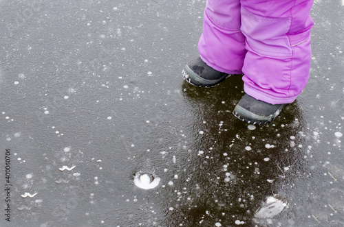 Children legs carefully walking on slippery road with frozen puddle covered with ice or thin ice of a pond. Concept of injury risk in winter and danger. Dangerously slippery for 