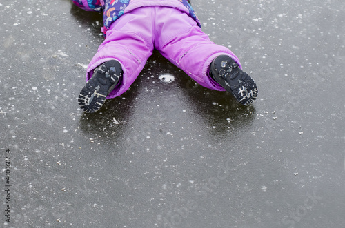 Child toddler falling on icy slippery pavement or sidewalk in winter. Slipped on the icy path. Concept of injury risk in winter. Dangerously slippery for pedestrian