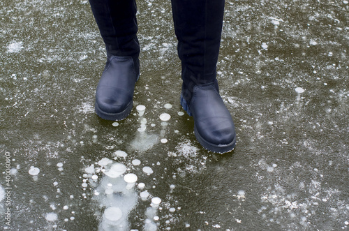 Female legs in black boots carefully walking on slippery road with frozen puddle covered with ice or thin ice of a pond. Concept of injury risk in winter and danger Dangerously slippery for pedestrian