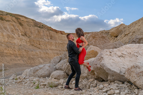 a strong young guy lifted a girl in a red dress with both hands
