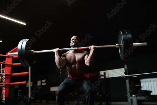 Heavyweight man training with a barbell. Bodybuilding trainer lifts heavy weights in the gym, preparing for competition
