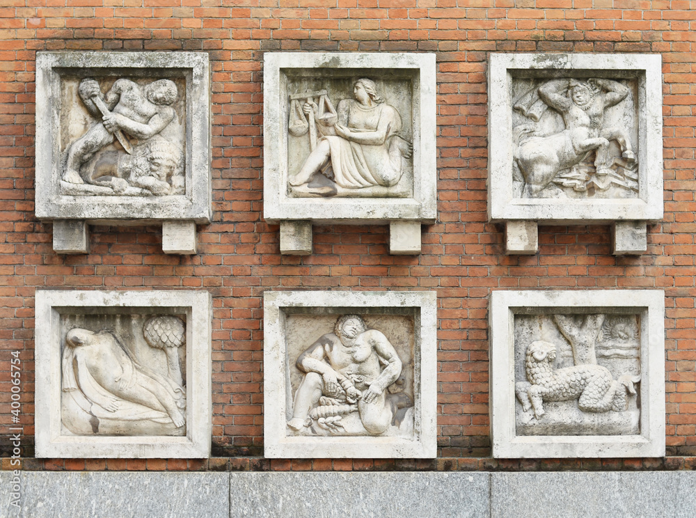 Six antique mythical scenes sculptured in stone in a street in Milan, Italy