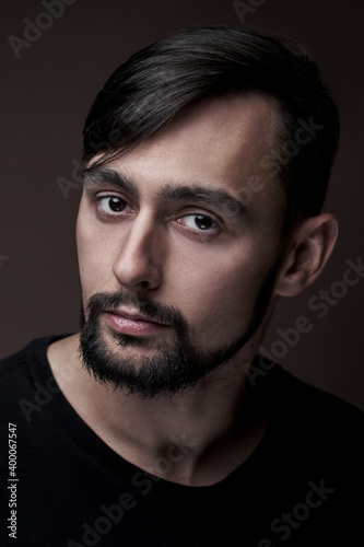 Portrait of handsome caucasian man with beard and stylish haircut in black clothes posing on brown background isolated in studio, fashion model looking at the camera