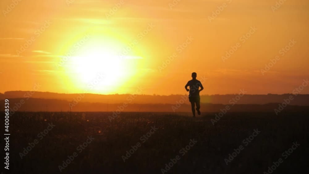 Running man silhouette in sunset time. Outdoor cross-country running. Athletic young man is running in the nature during golden sunset. Healthy lifestyle.