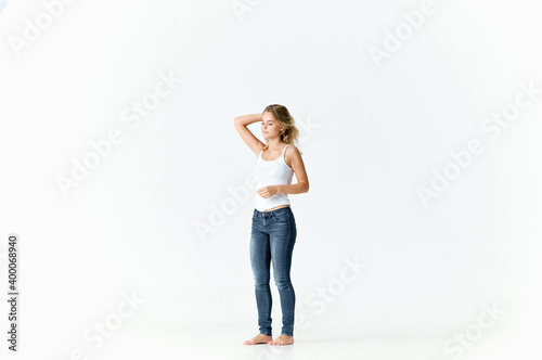 a slender woman in jeans and a white T-shirt barefoot on a light background in full growth 
