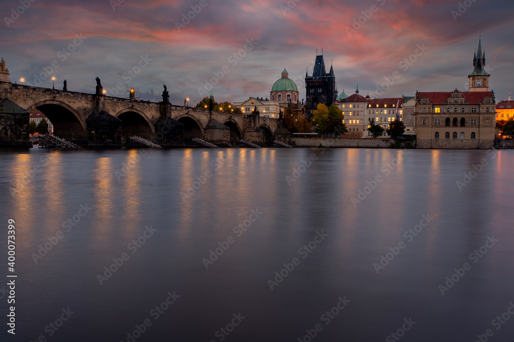 .Stone Charles Bridge on the Vltava River at sunset and colorful clouds and lights on the bridge in the early evening in the center of Prague