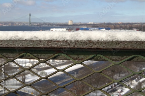 Winter in the city , snow on a metal fence with a city skyline street and a bridge view in a soft bokeh background