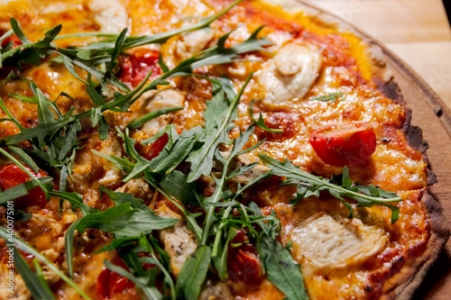 pizza with arugula, meat and tomatoes on a wood plate for restaurant menu