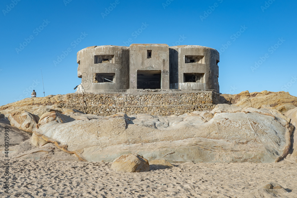 Bunker militar abandonado sobre una roca en la playa contra cielo azul. Desde la playa de Atlanterra, Zahara de los Atunes, Cádiz, Andalucía, España.