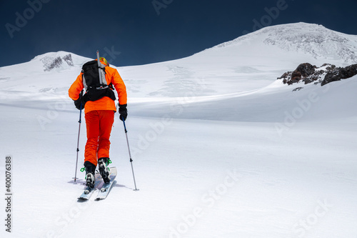 A mountaineer skier with a backpack, an ice ax, skis and poles, ascend on a ski tour to Mount Elbrus. Backcountry and freeride skiing concept