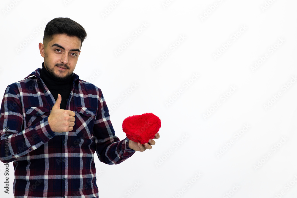 Handsome young male model. He is holding a gift box in the shape of a heart. He is wearing a dark checkered shirt.