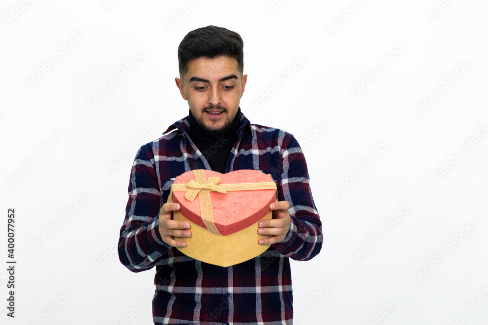 Handsome young male model. He is holding a gift box in the shape of a heart. He is wearing a dark checkered shirt. Handsome young male model. He is holding a gift box in the shape of a heart. He is wearing a dark checkered shirt.