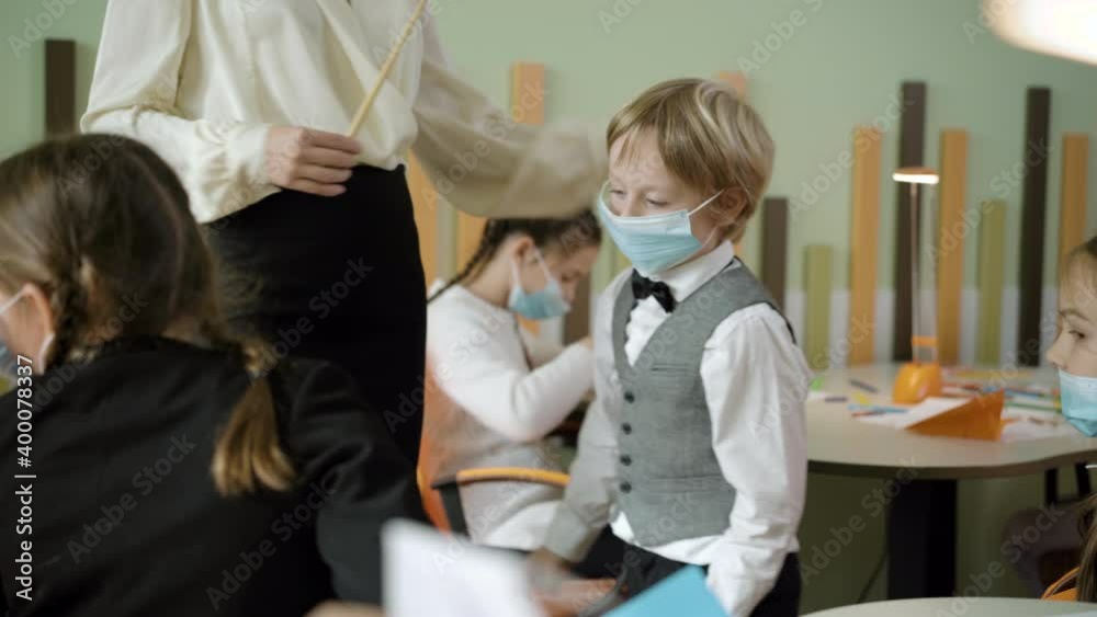 Cute Caucasian boy in Covid face mask talking to unrecognizable slim teacher and launching paper plane. Positive arts lesson in public school on coronavirus pandemic. Education and lifestyle. Cute Caucasian boy in Covid face mask talking to unrecognizable slim teacher and launching paper plane. Positive arts lesson in public school on coronavirus pandemic. Education and lifestyle.