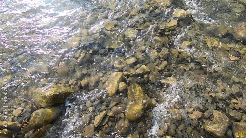 Natural background. Water flows over stones at the bottom of a shallow river Natural background. Water flows over stones at the bottom of a shallow river