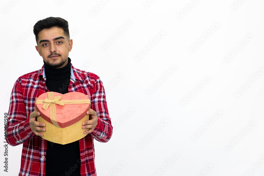 Young male holding a heart-shaped gift box in his hand. Wearing a striped shirt. Isolated image and white background. Young male holding a heart-shaped gift box in his hand. Wearing a striped shirt. Isolated image and white background.