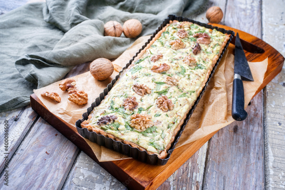 Fototapeta premium Traditional French Autumn walnut spinach tarte served as close-up in a backing form on an Modern design wooden board