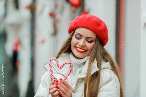 Christmas. Close-up portrait of a beautiful young woman in red biret holding a Christmas candy. Holidays. photo