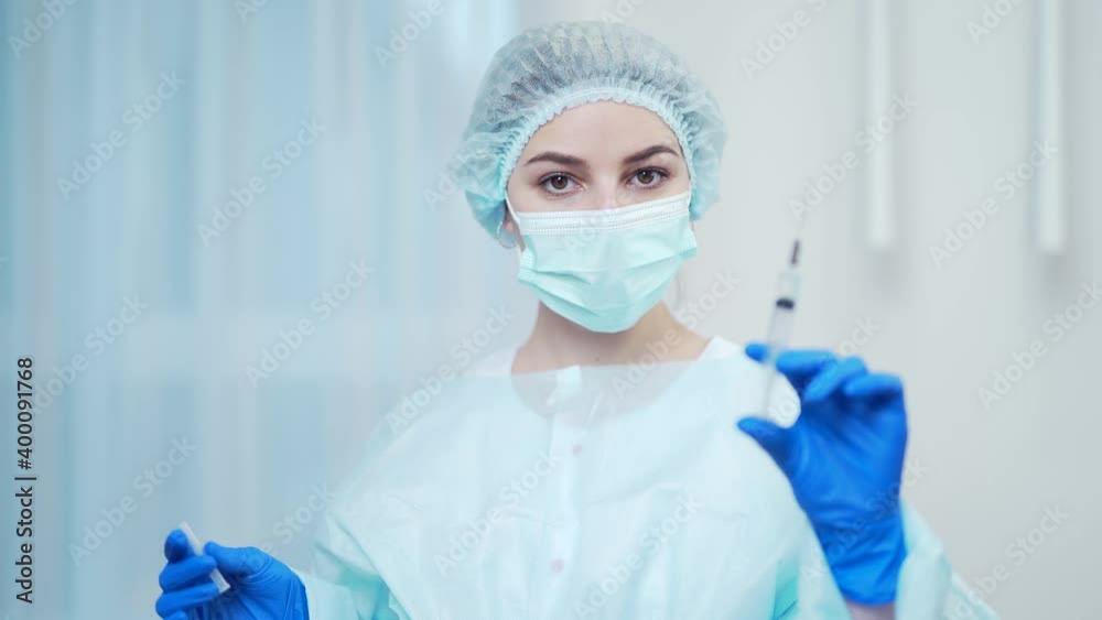 Portrait woman in a medical uniform with a protective mask and gloves holding a syringe for vaccination. Female family doctor therapist ready to give an injection. In the hospital or at home indoors