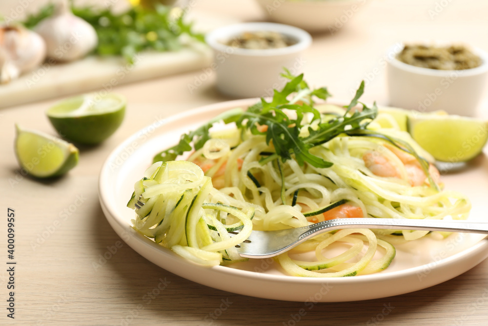 Tasty zucchini pasta with shrimps and arugula served on wooden table, closeup