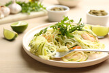 Tasty zucchini pasta with shrimps and arugula served on wooden table, closeup