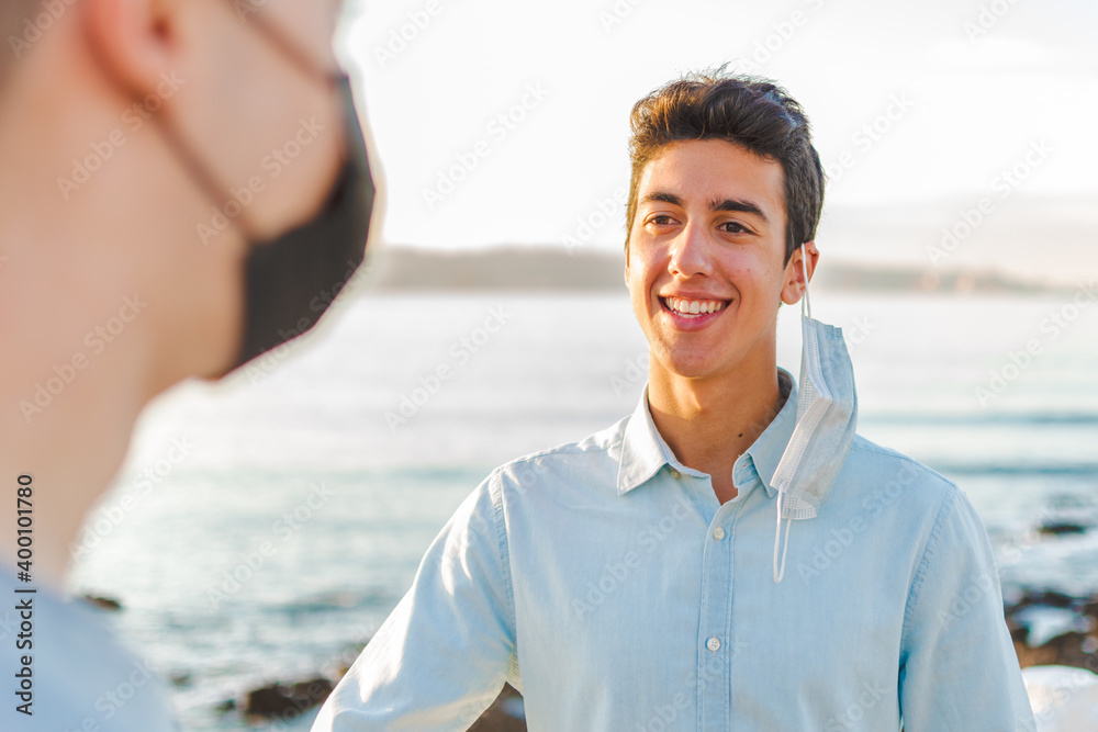 Obraz premium Young man smiling with surgical mask talking to a blurred person next to the sea