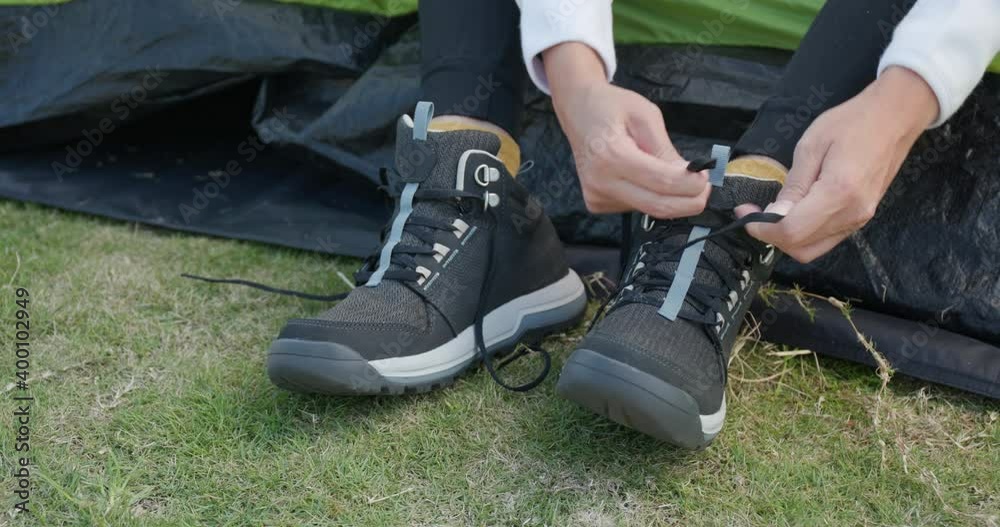 Woman tying her shoes after hiking at camping site Woman tying her shoes after hiking at camping site