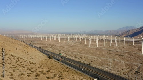 Drone flying sideways overlooking highway inbetween of huge wind farm and wind turbines near Palm Springs in the Mojave Desert, California, USA.