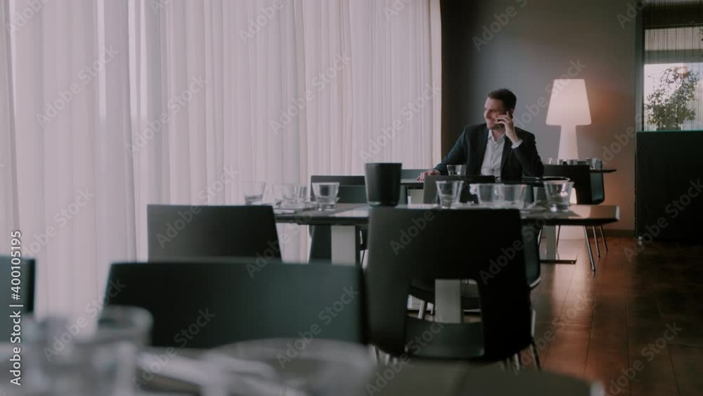 Businessman sitting in an empty restaurant and smiling while talking on the phone Businessman sitting in an empty restaurant and smiling while talking on the phone