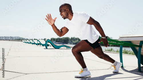Black guy in white t-shirt and black shorts exercising and screaming outside with elastic tape.