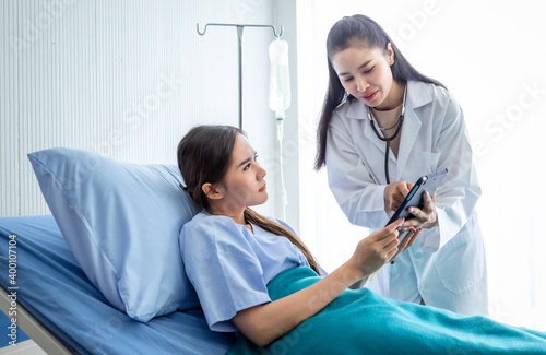 Obraz na płótnie Asian female doctor therapeutic advising with tablet to young female patient on Bed in hospital background. w salonie