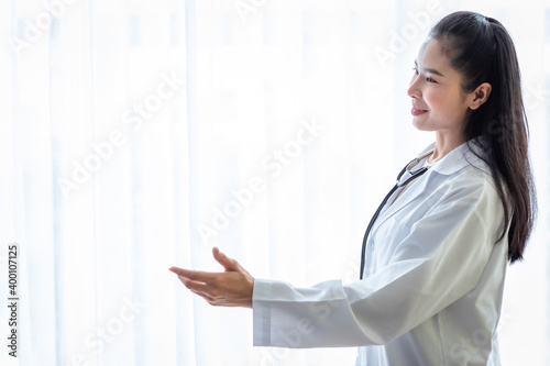 Portrait of asian young female doctor smiling face with stethoscope pointing with hand with copy space in hospital background. Free Download Portrait of asian young female doctor smiling face with stethoscope pointing with hand with copy space in hospital background. - GFXLoad