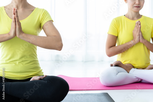 Two young Asian women workout practicing yoga in yellow dress or pose with a trainer and practice meditation wellness lifestyle and health fitness concept in a gym.