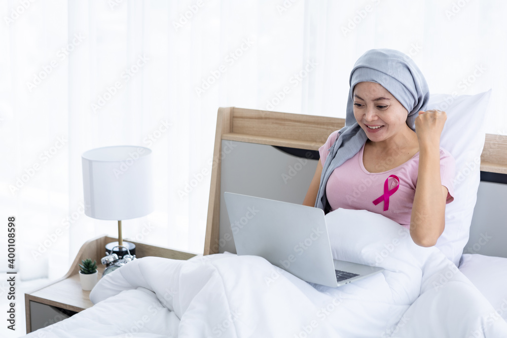 a asian women disease mammary cancer patient with pink ribbon wearing headscarf After treatment to chemotherapy with working business at laptop on bed In the bedroom at the house,healthcare,medicine a asian women disease mammary cancer patient with pink ribbon wearing headscarf After treatment to chemotherapy with working business at laptop on bed In the bedroom at the house,healthcare,medicine