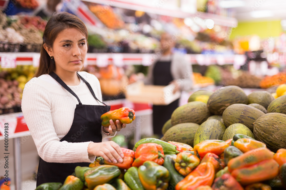 Supermarket employee lays out ripe bell peppers on the shelves
