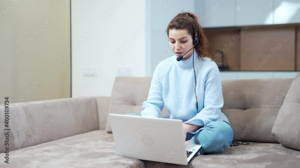 Online distance learning. Woman freelancer at home communicates via internet. The teacher explains remotely. young adult student girl sitting on sofa with headset and laptop and talking to webcam. Online distance learning. Woman freelancer at home communicates via internet. The teacher explains remotely. young adult student girl sitting on sofa with headset and laptop and talking to webcam.