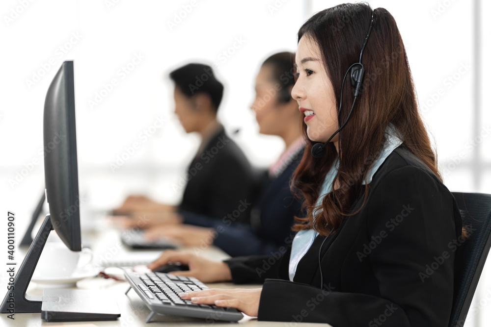 Group of happy asian smiling call center business operator customer support team phone services agen working and talking with headset on desktop computer at call center Group of happy asian smiling call center business operator customer support team phone services agen working and talking with headset on desktop computer at call center